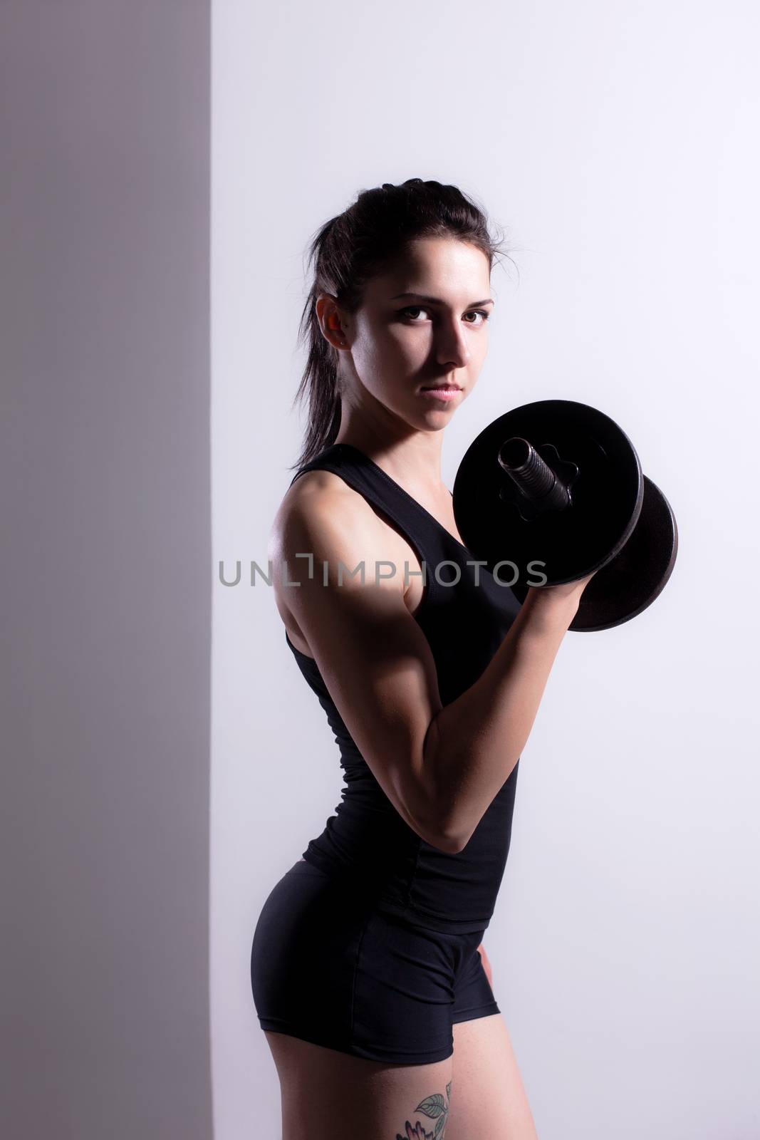Fitness girl posing and lifting weights, looking at camera