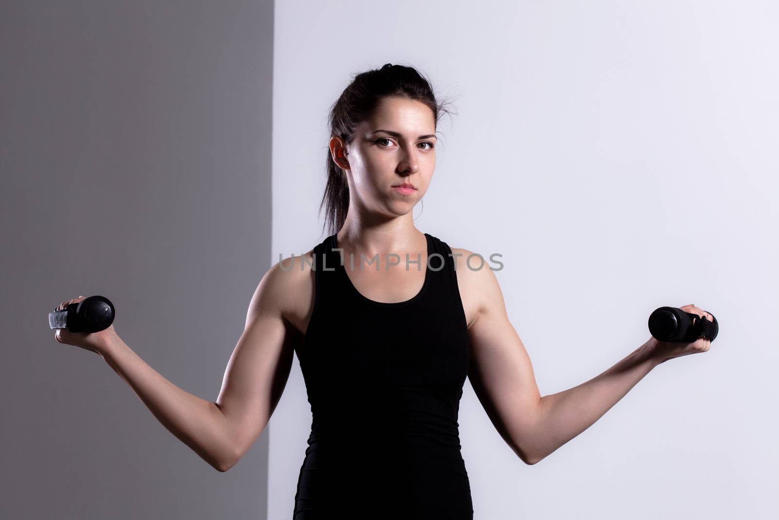 Fitness girl posing and lifting weights, looking at camera
