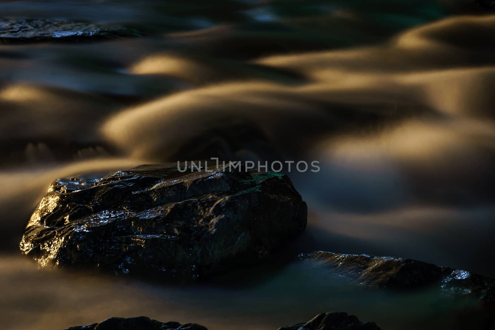 Long exposure shot of fast running water from river flowing over rocks at night