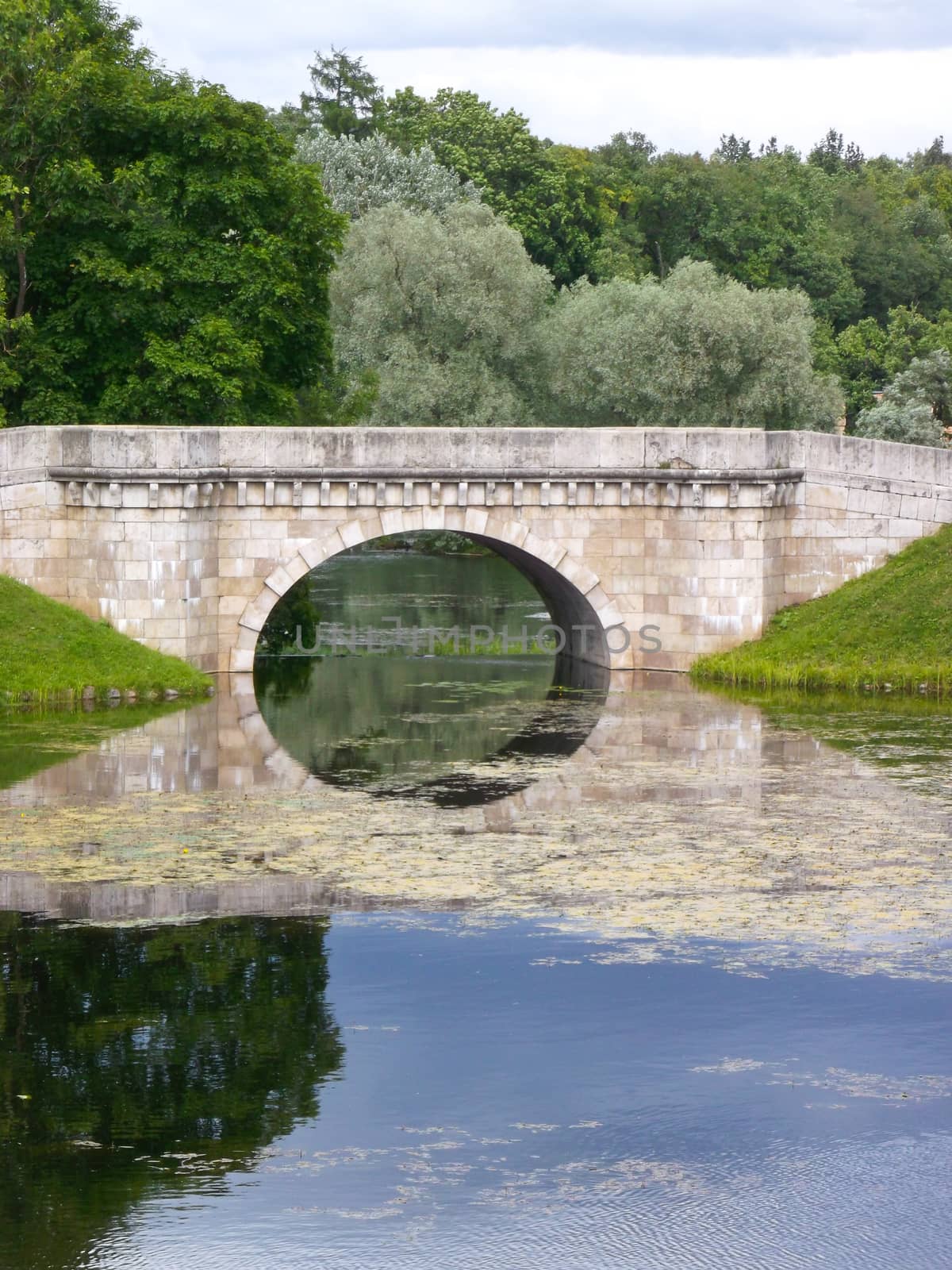 a stone bridge over the river on background of blue sky and green trees