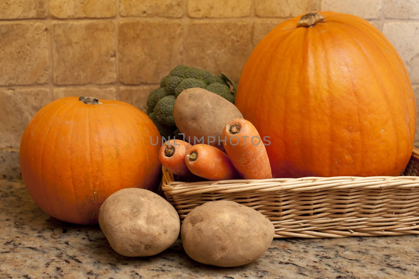 Harvest of fresh fall or autumn vegetables in a shallow wicker basket on a granite counter including carrots, potatoes, broccoli and pumpkins