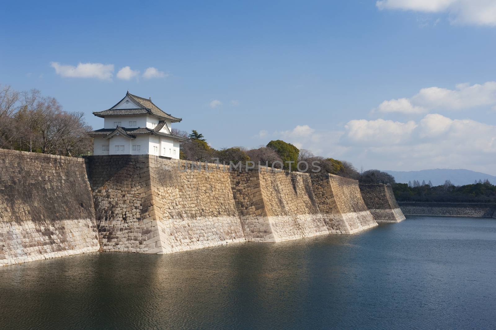 Exterior walls of the Osaka-jo castle, Japan with a small pagoda overlooking the calm water of the surrounding moat, a popular tourist attraction and museum