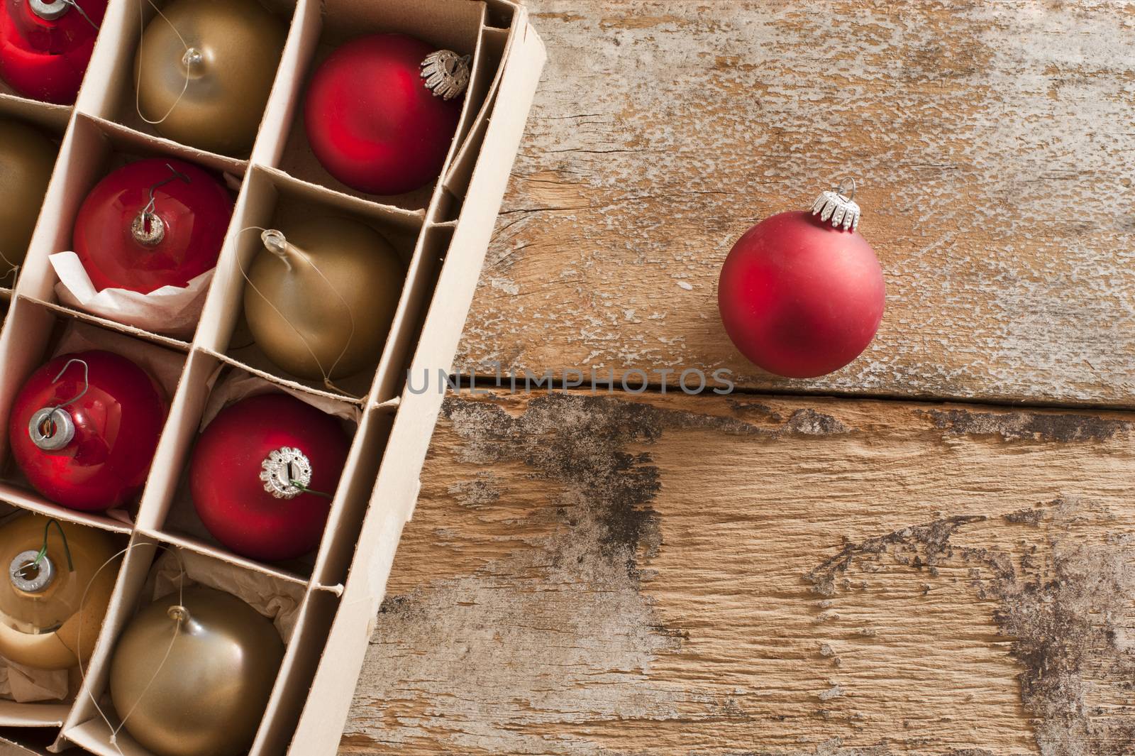 Boxed assortment or red and gold Christmas baubles with a single red one outside the packaging on a rustic wooden background with copy space