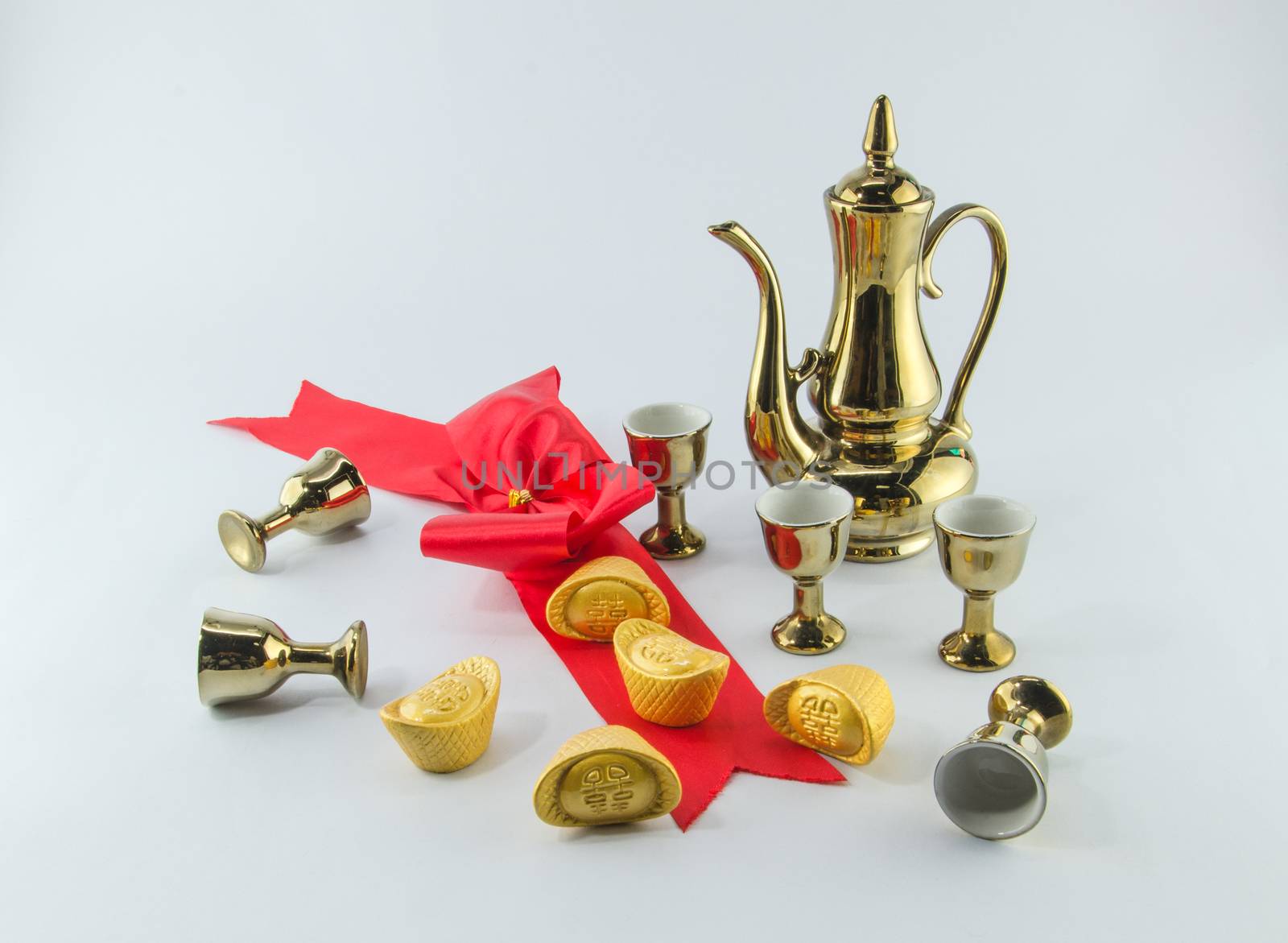 Gold ingot Red ribbon bow Gold jug Tea glass on white background.