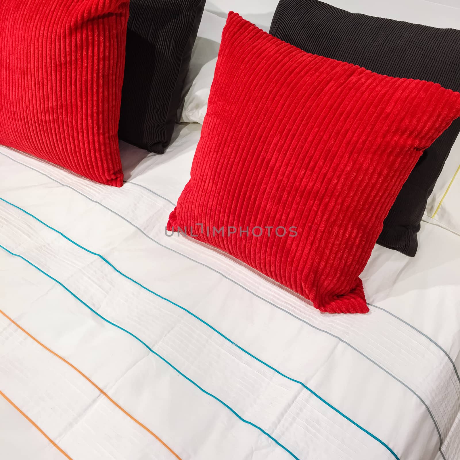 Red and black velveteen cushions on a bed with striped bed linen.