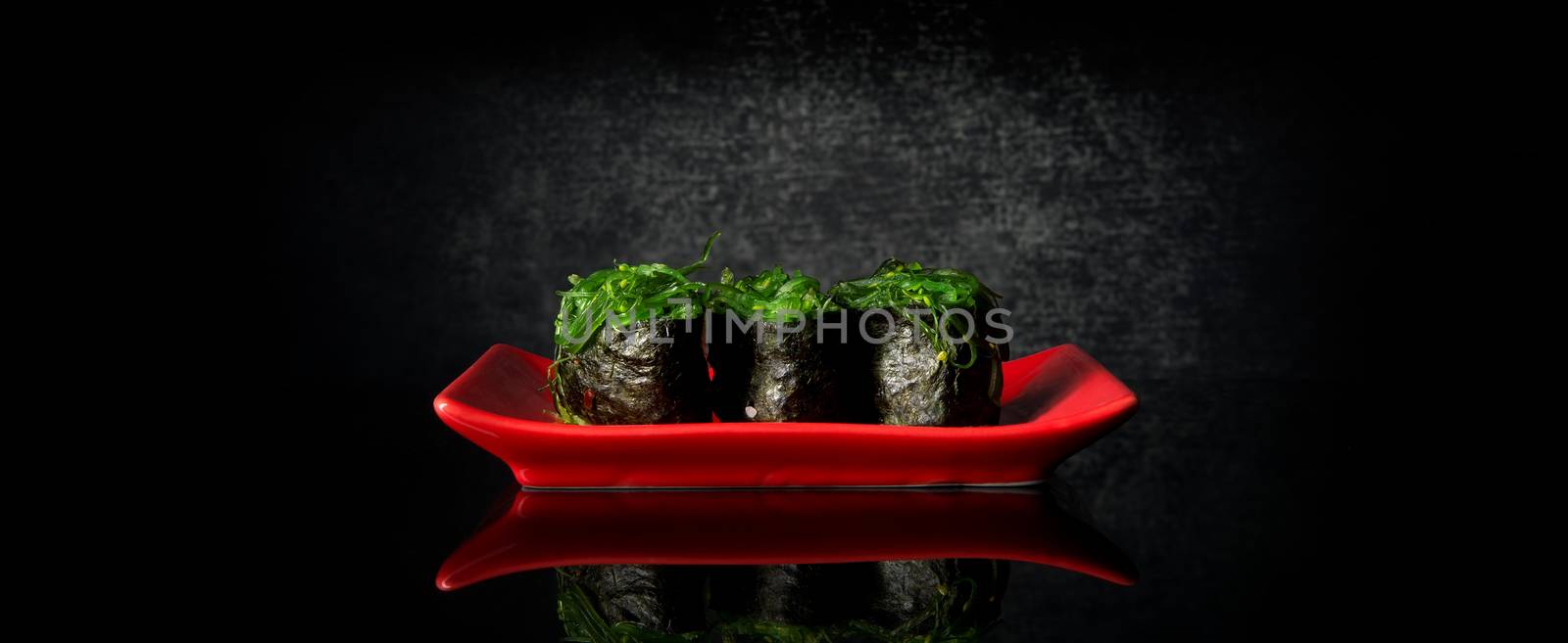 Rolls with chuka algae on red dish and black background