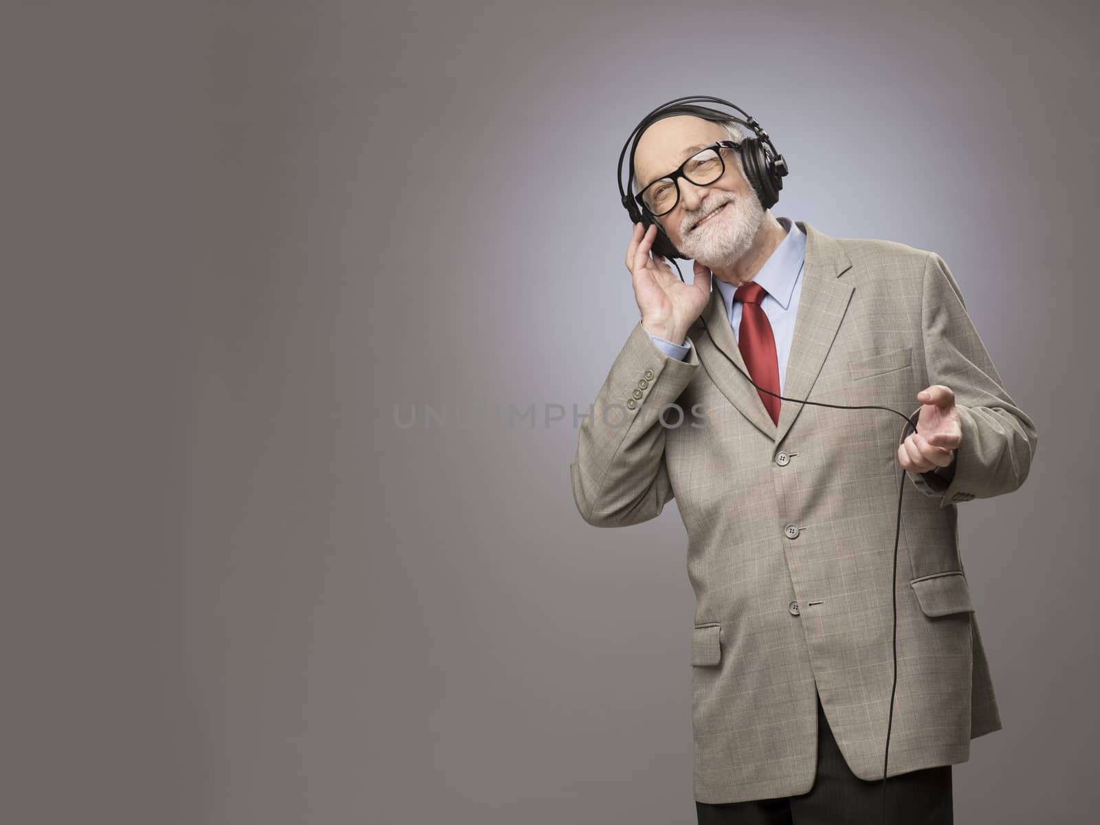 Portrait of senior man in headphones listening music, studio shot on gray background