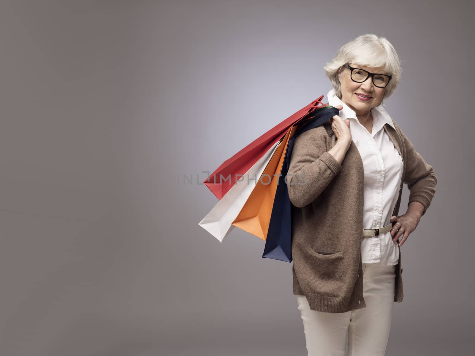 Studio portrait of happy senior woman with shopping bags