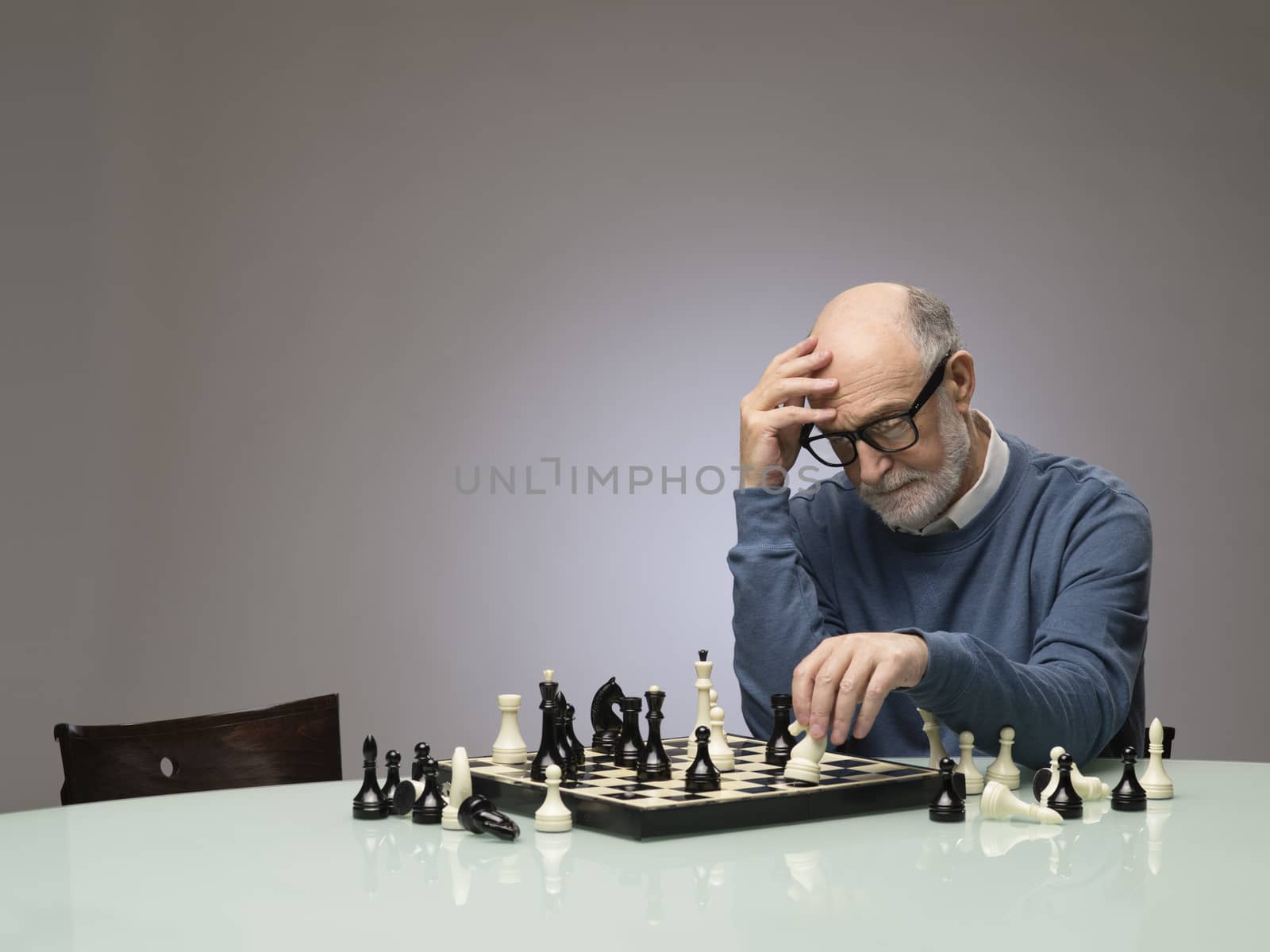 Senior man thinking over his move in chess, studio shot on gray background with copy space