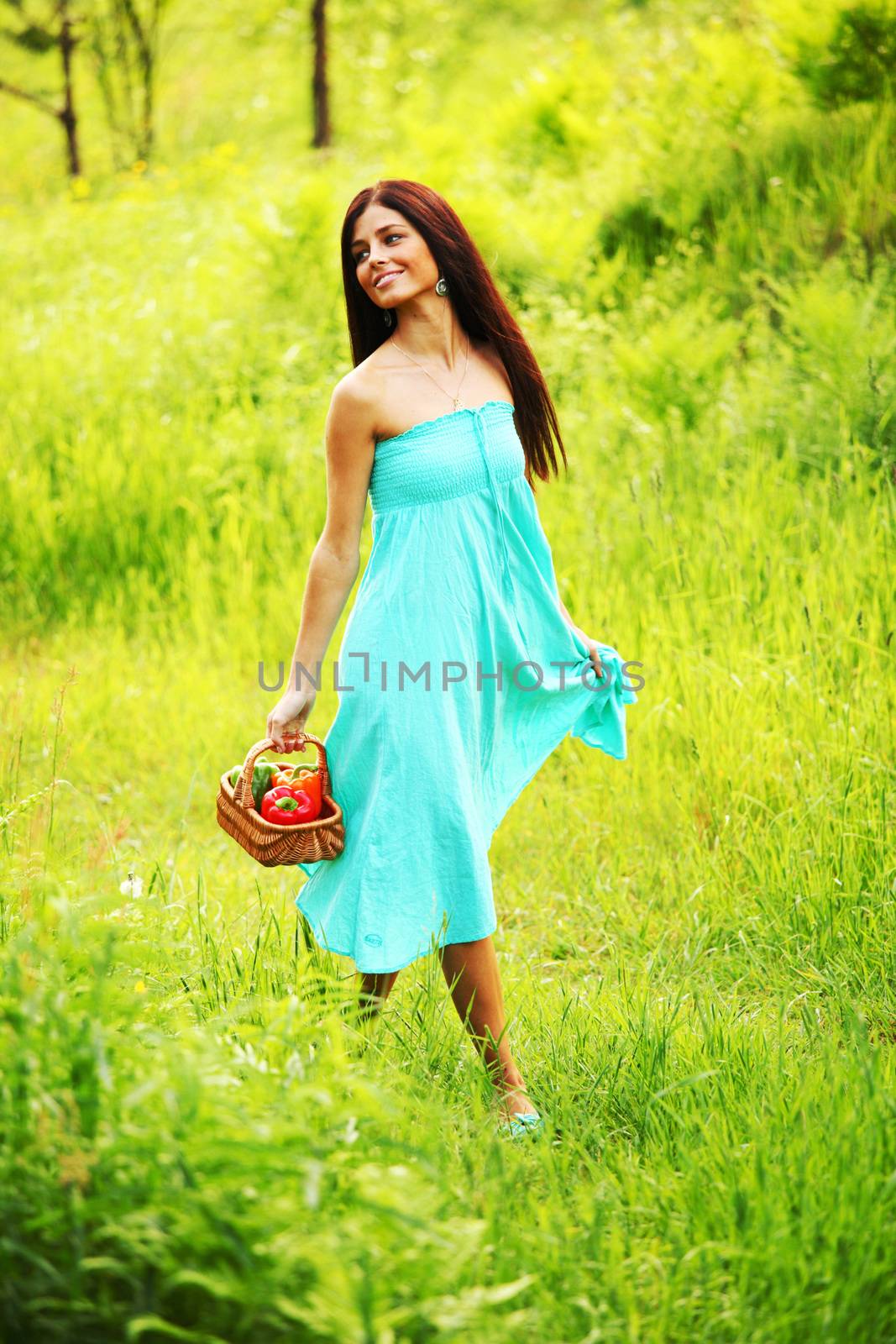 Beautiful young woman walking on summer grass field with basket of paprica