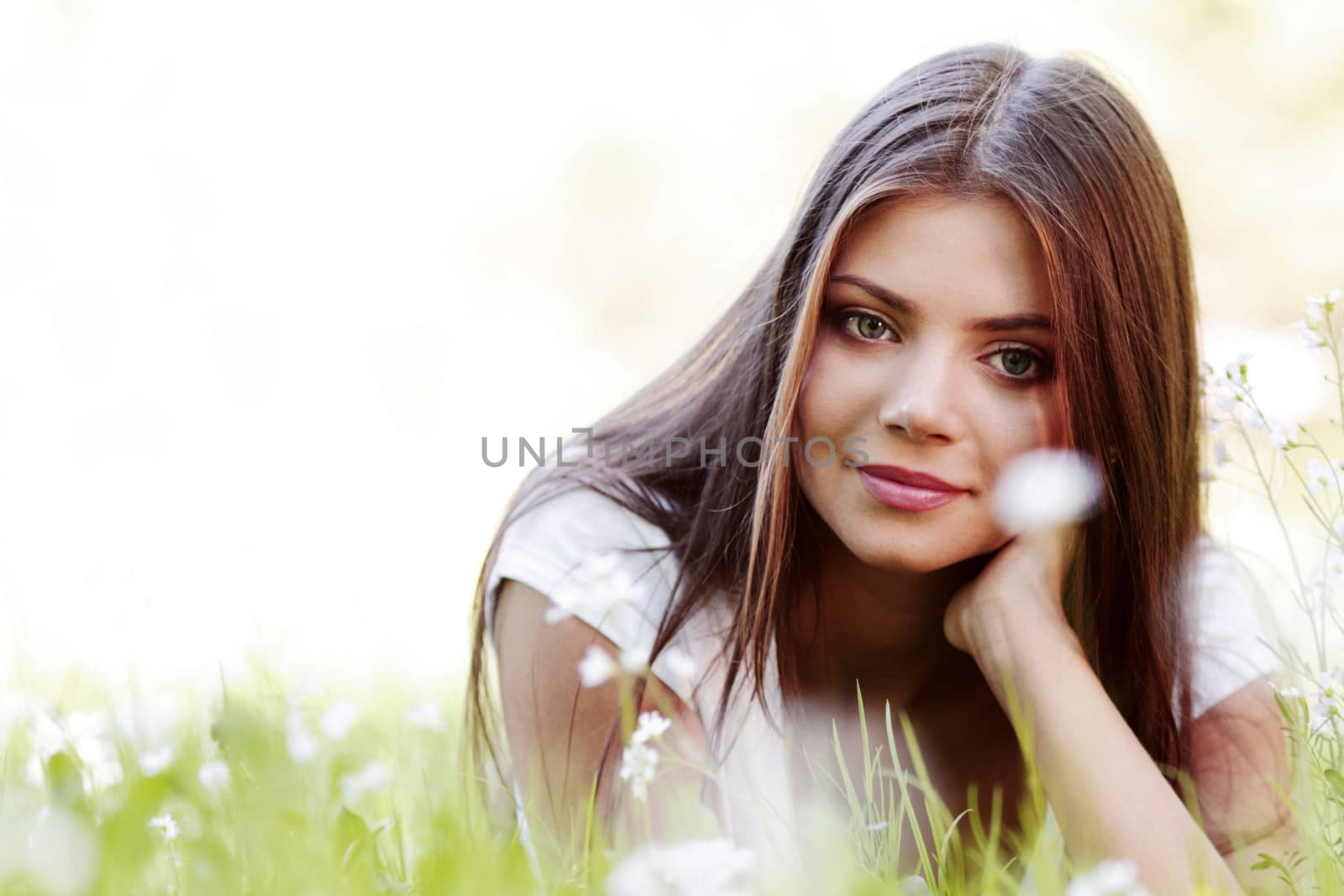 Pretty brunette girl laying on grass with white  flowers around her