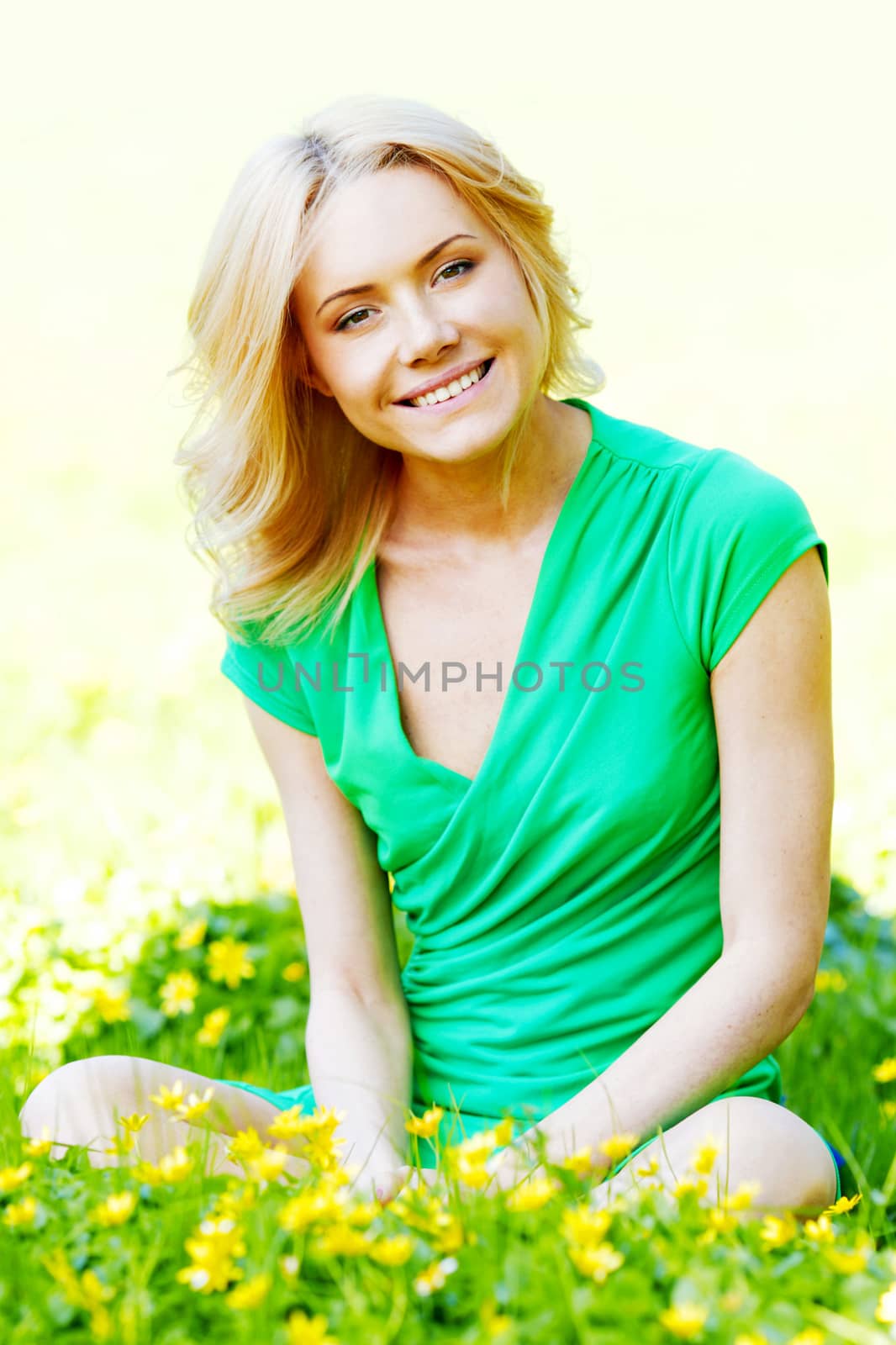 Beautiful young blond woman sitting on grass in park and enjoyng flowers