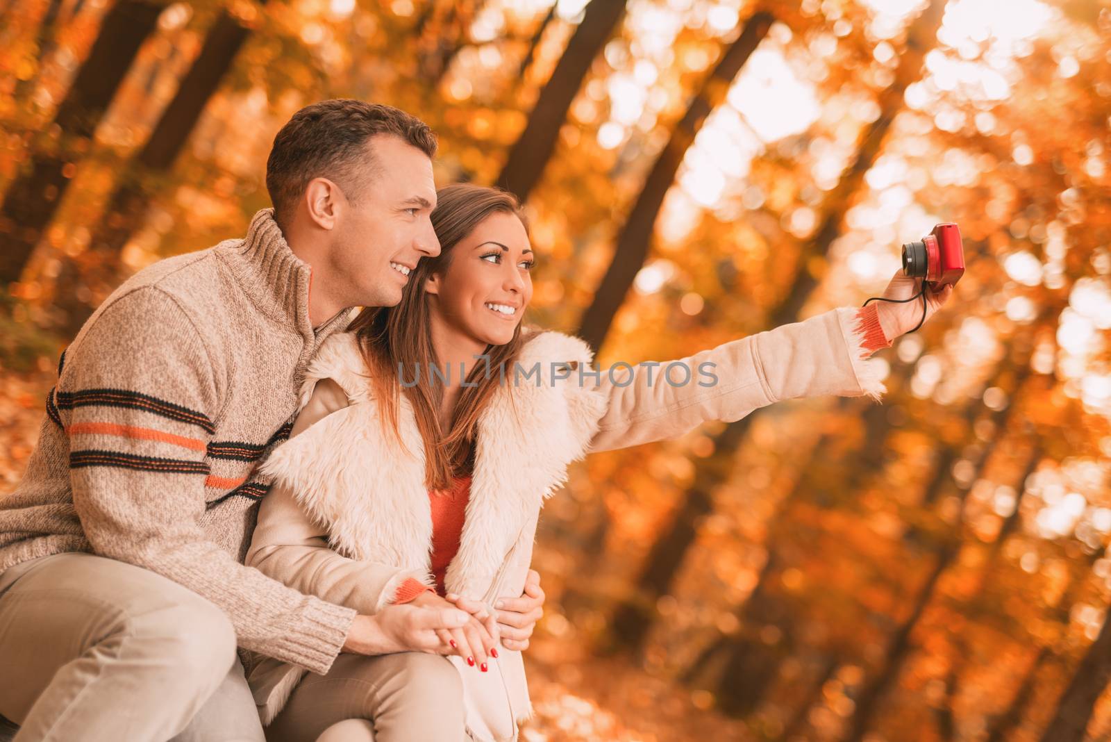 Beautiful smiling couple enjoying and taking selfie in forest in autumn.