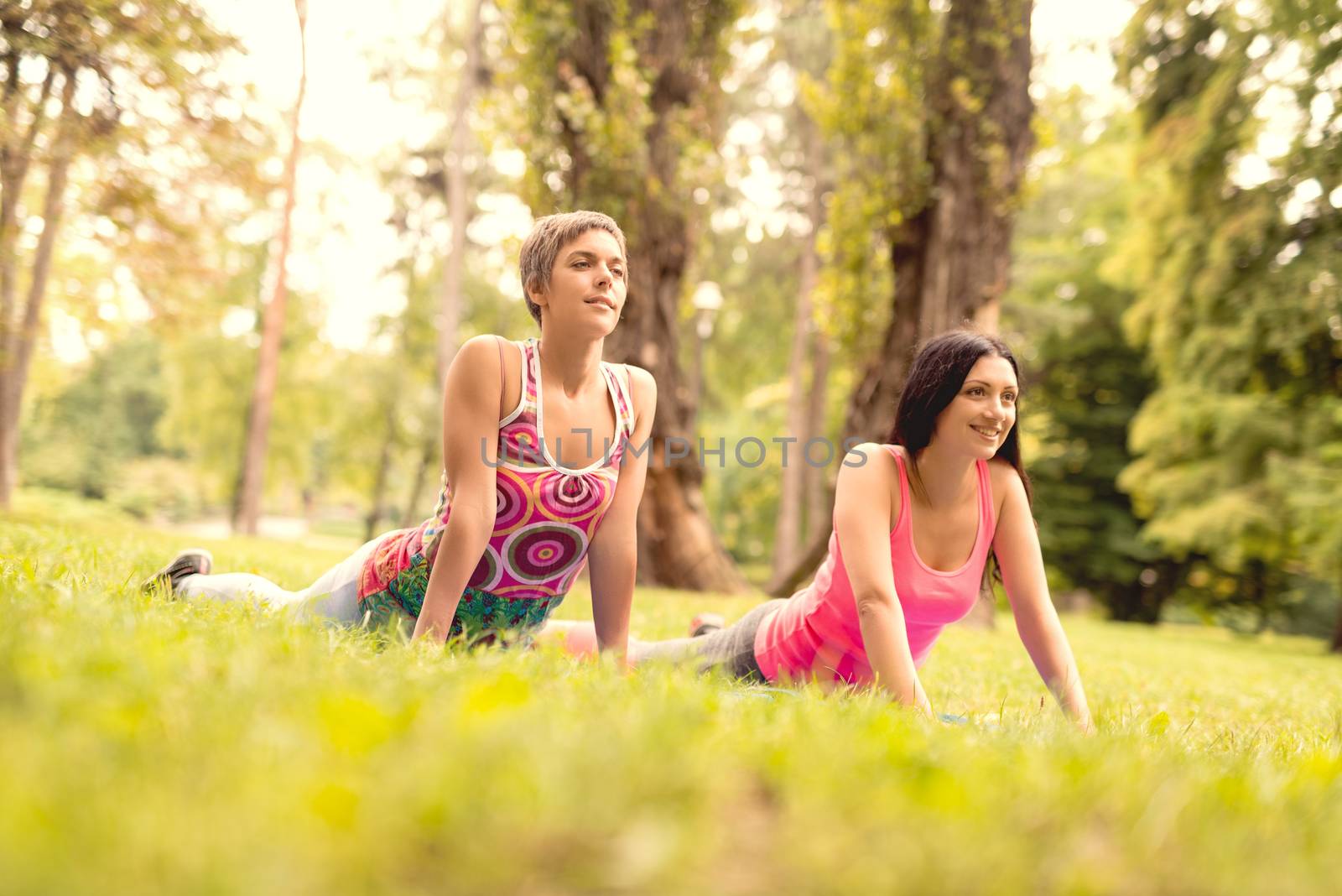 Two beautiful women doing stretching exercise in the park. 