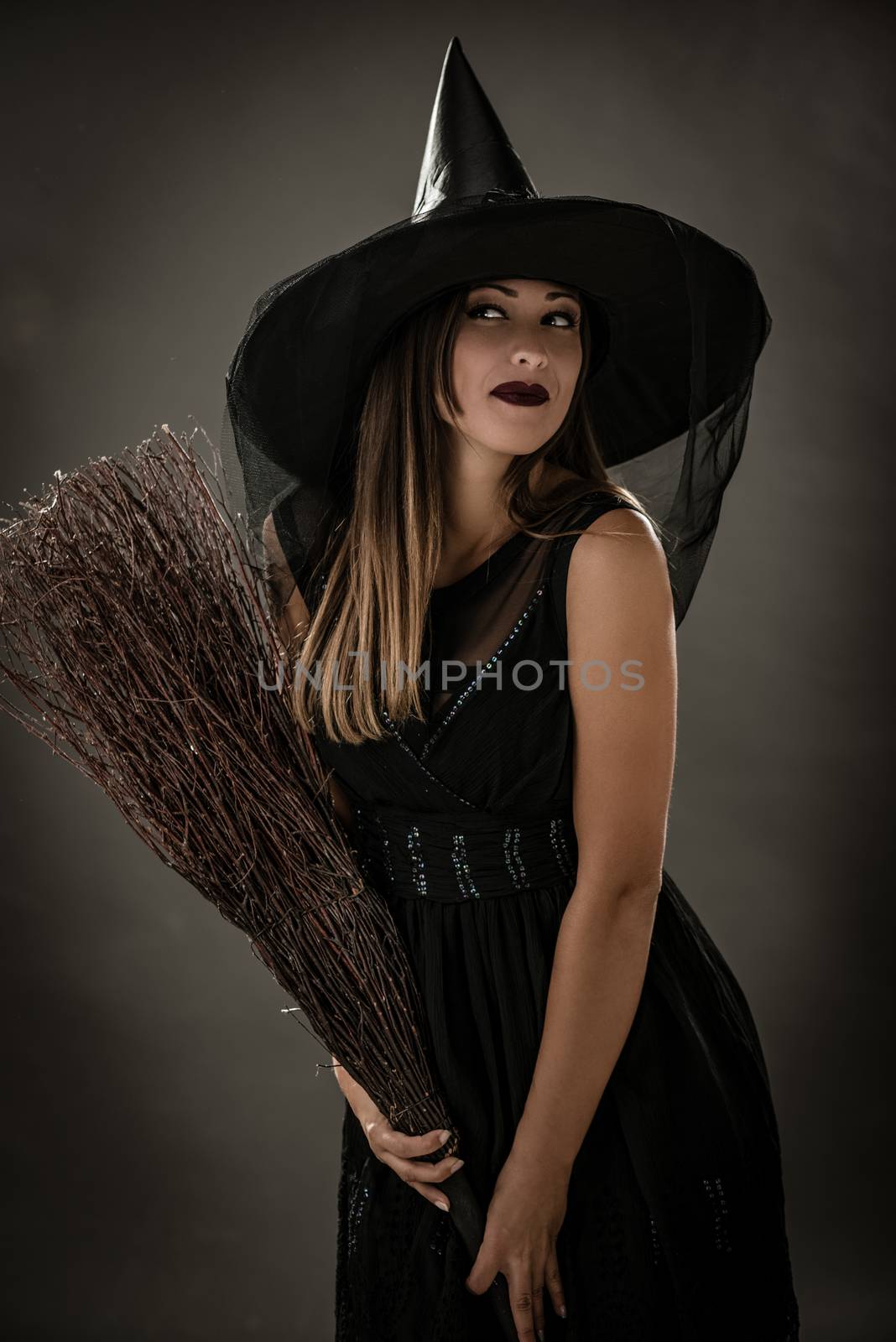 Young woman dressed like a witch. She is in dark clothing and holding a broom. 