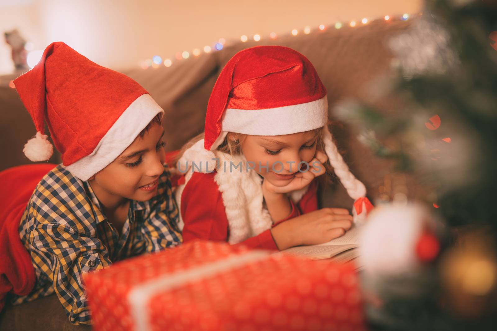 Cute smiling sister and brother reading a book at the home in a Christmas time. They are waiting for a Santa Claus.