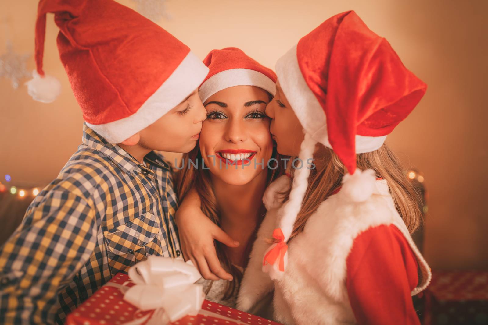 Cute smiling girl and boy give a present to their happy mother for Christmas or New Year. They are kissing and embraced mom.