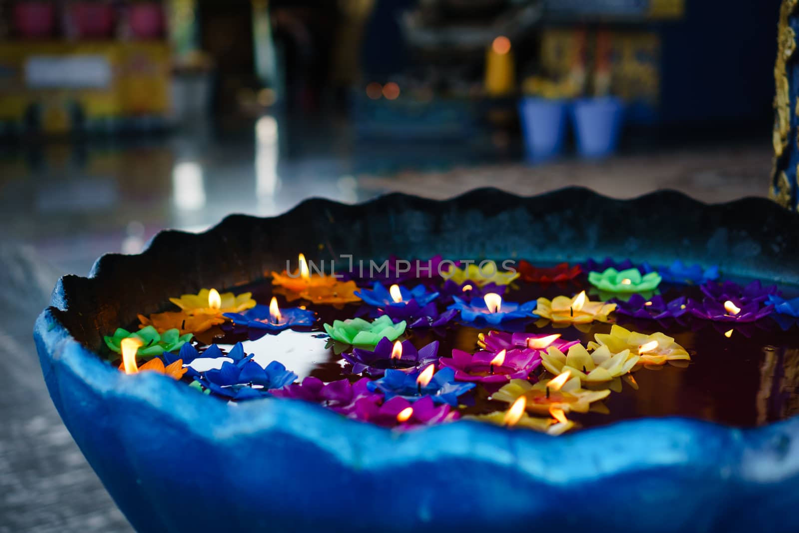 Multiple colored flower shaped candles floating in blue water-font