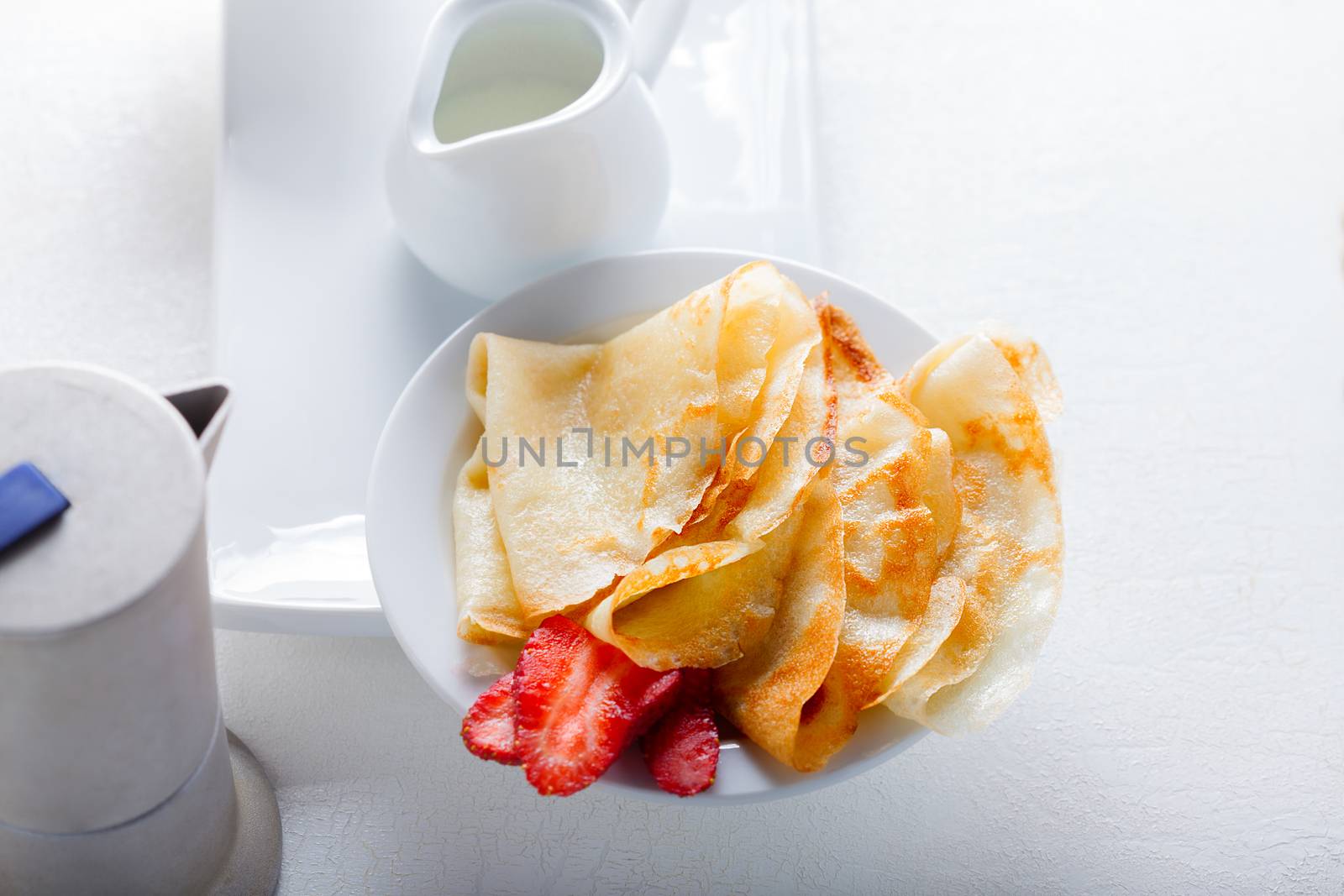 Crepes with strawberries and coffee on a white plate