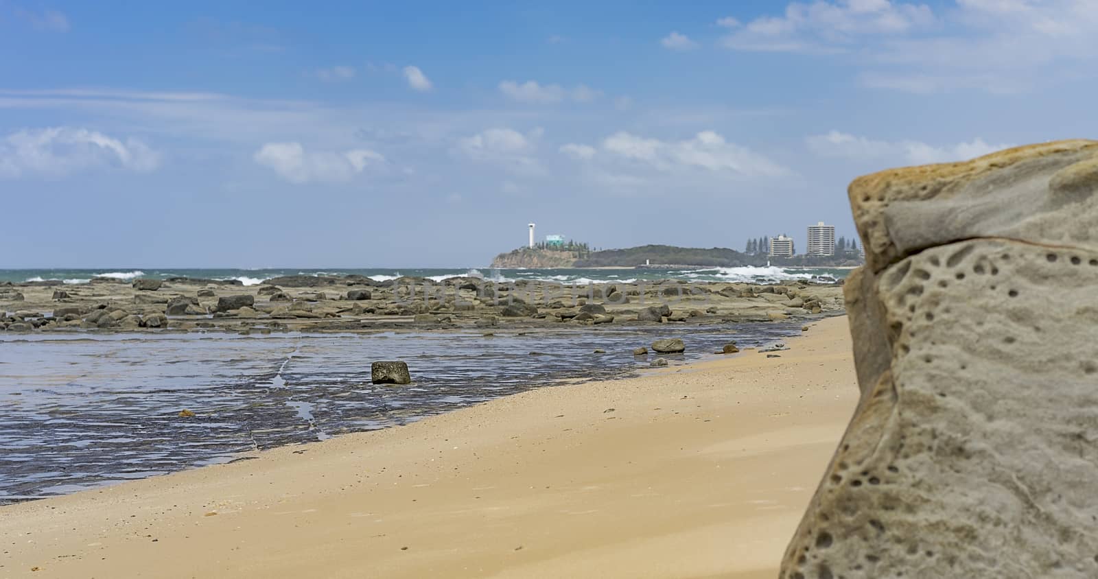 Australian beach panorama with sandy foreground,  rocks, reef, crashing waves, ocean, horizon and blue sky