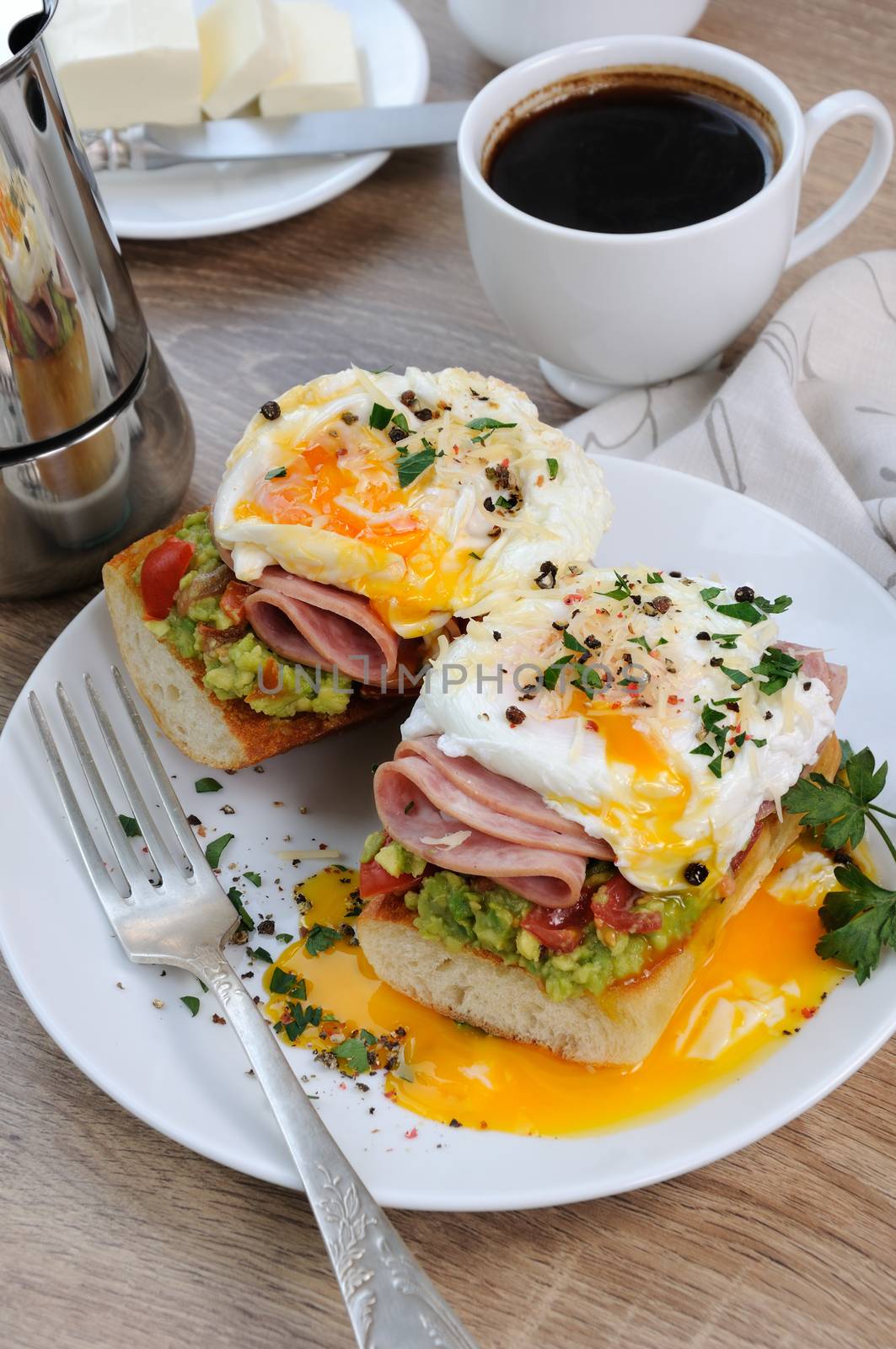 poached  eggs with avocado, tomatoes, slices of ham on a baguette for breakfast