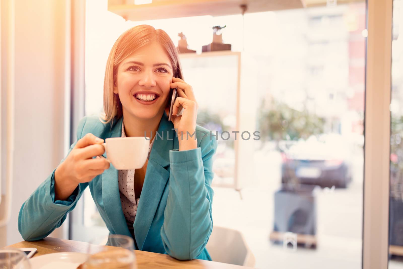 Young smiling businesswoman on a break in a cafe. He is drinking coffee and using smart phone. 