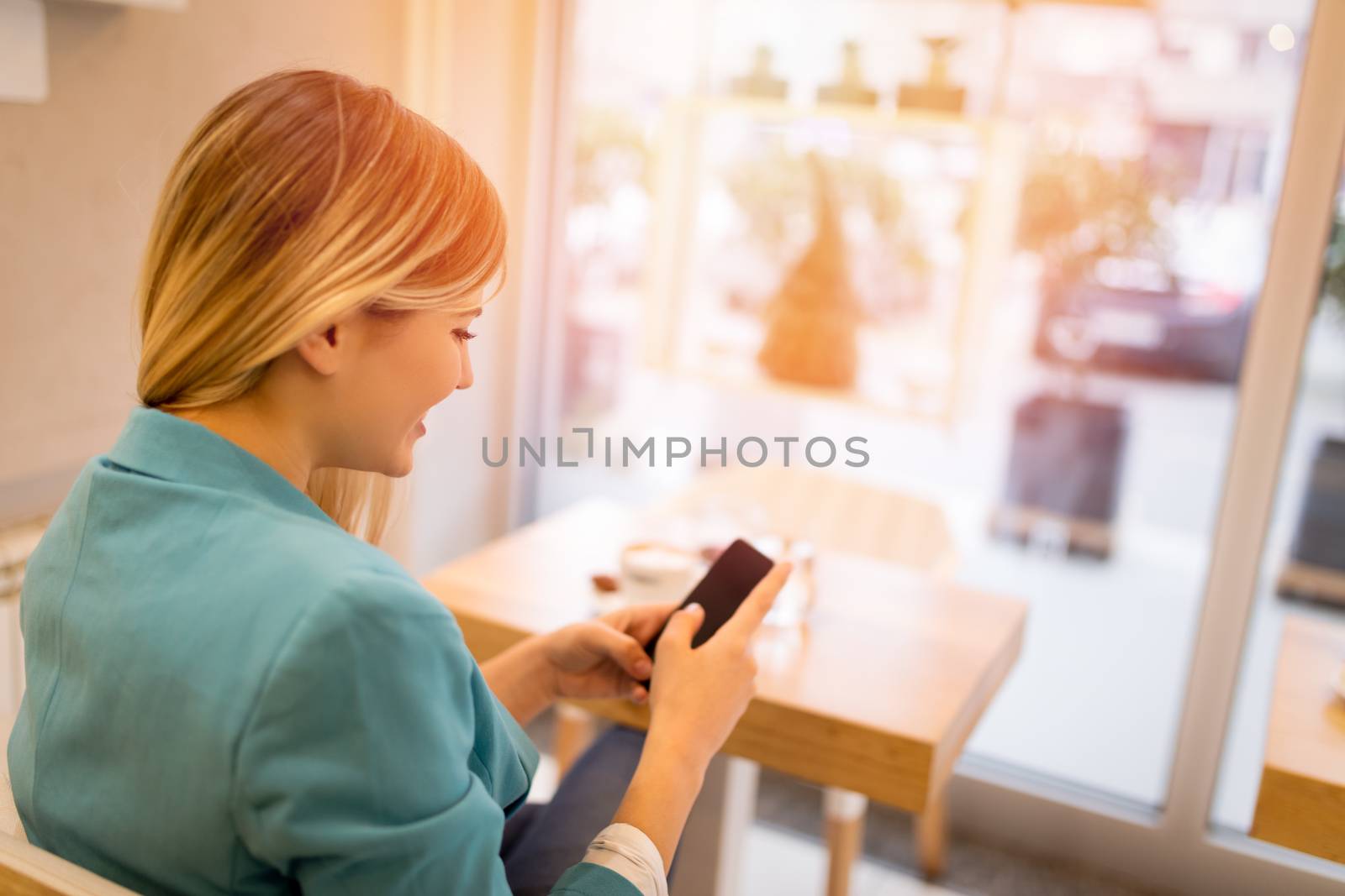 Beautiful young smiling woman using smart phone in a cafe.
