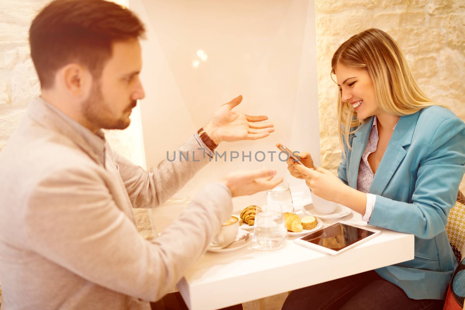 Young smiling businesspeople on a break in a cafe. Woman using smart phone with smiling on her face. Furious man talking for her. Selective focus.