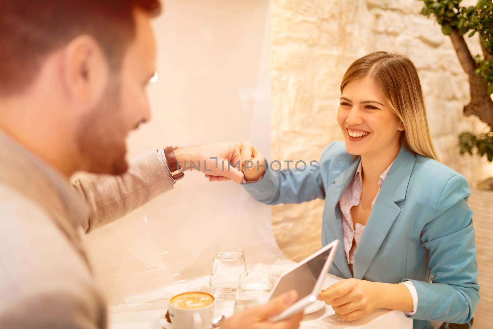 Young businesspeople on a break in a cafe. They are celebrating successful deal with fist bump. Selective focus. Focus on busineswosman.