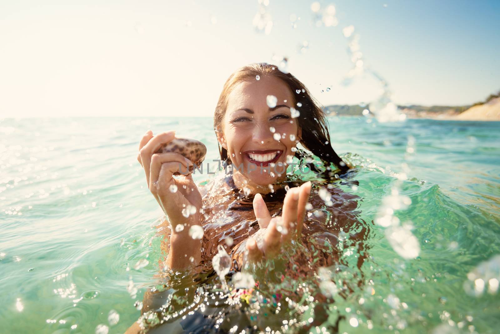 Beautiful young woman having fun and enjoying in the sea, on the beach. They are holding shell.