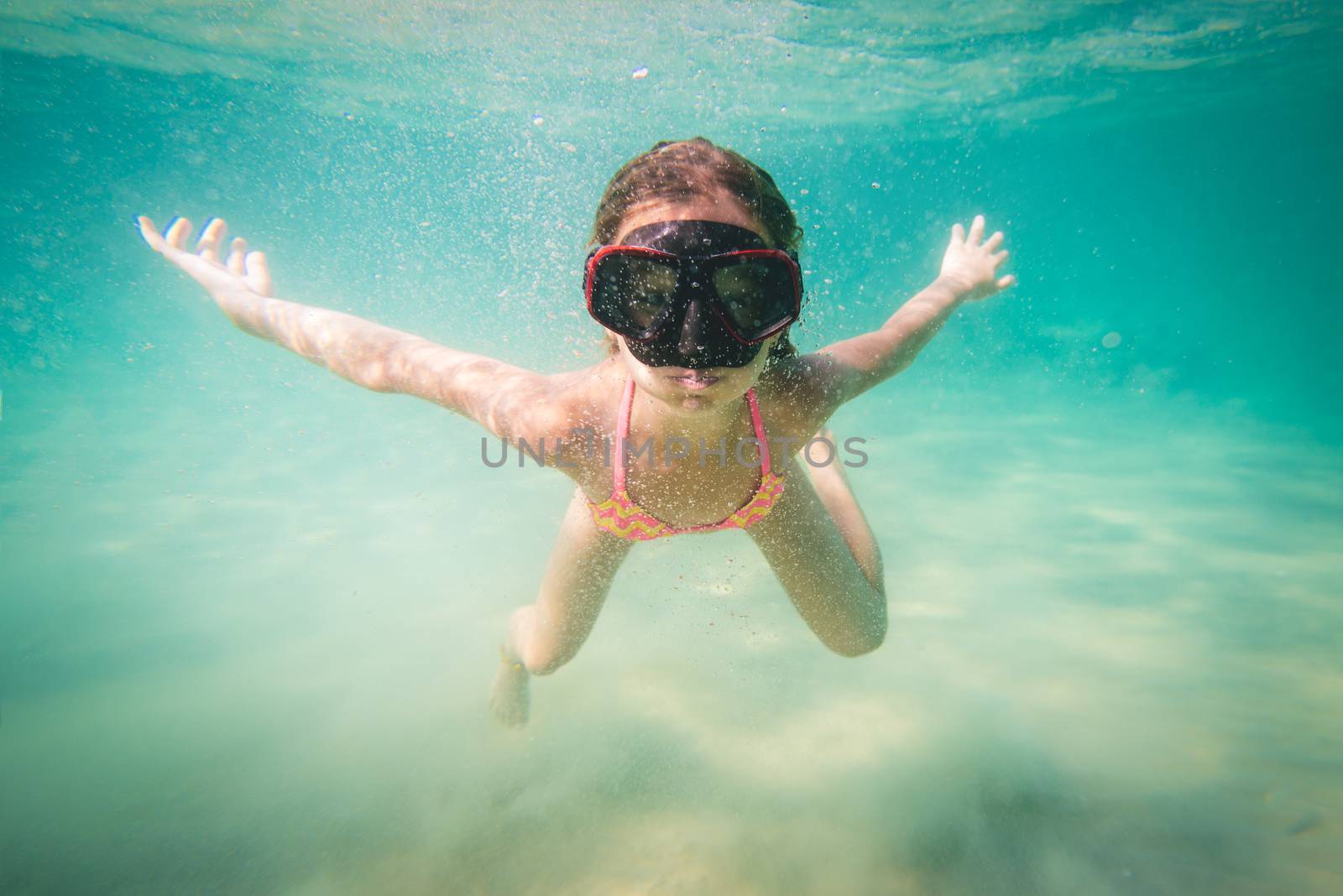 Beautiful little girl diving with mask underwater in the sea.