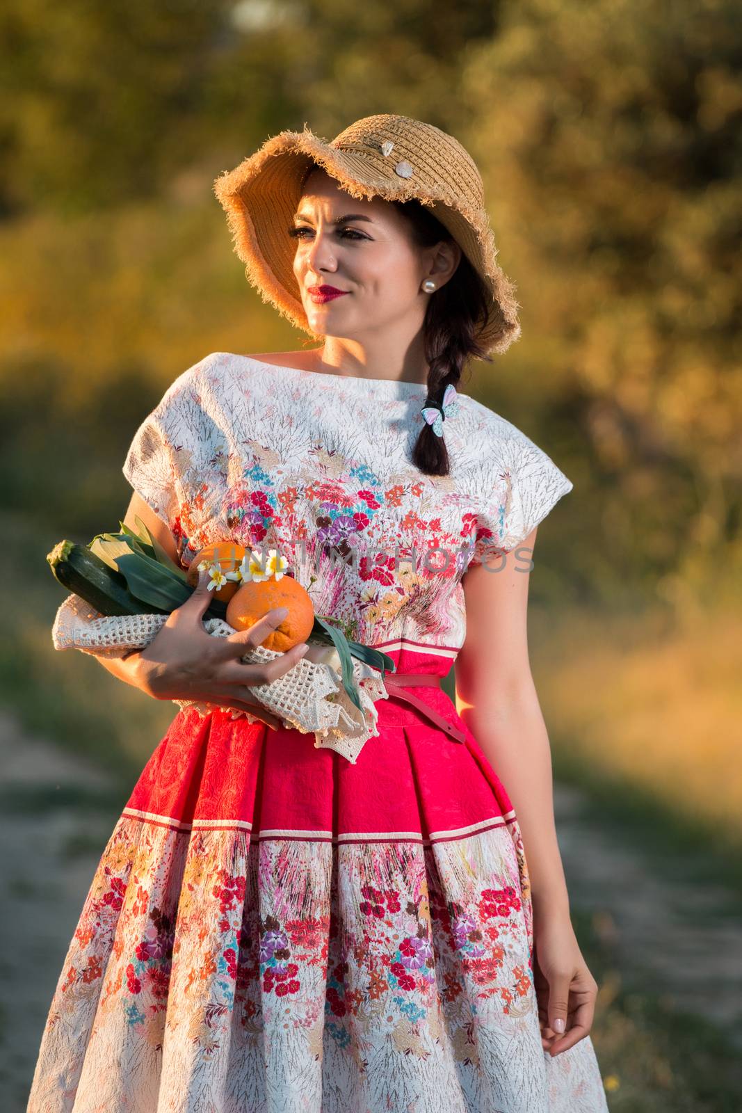 Vintage girl on the countryside with wicker hat gathering groceries.