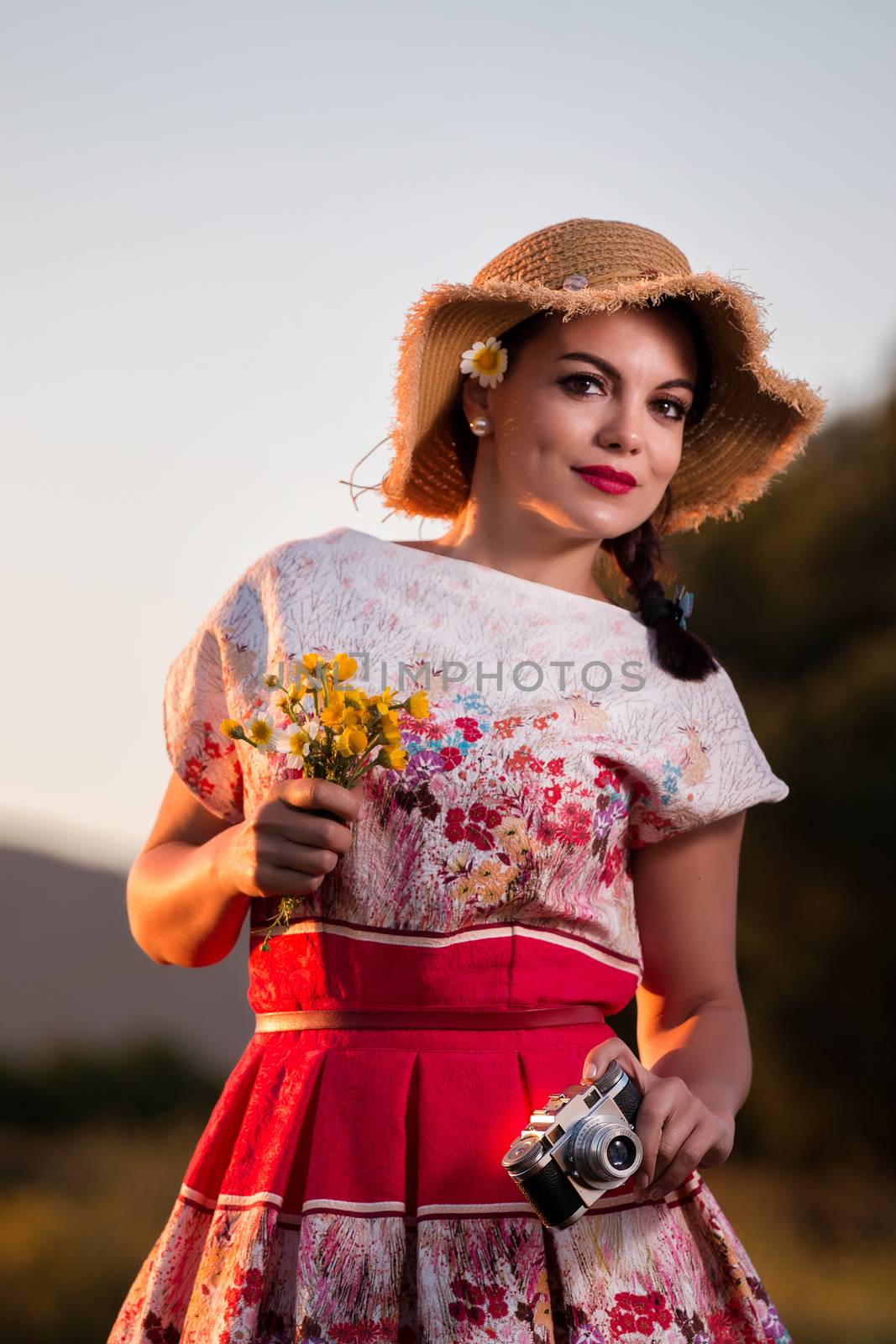 Vintage girl on the countryside with wicker hat with retro camera.