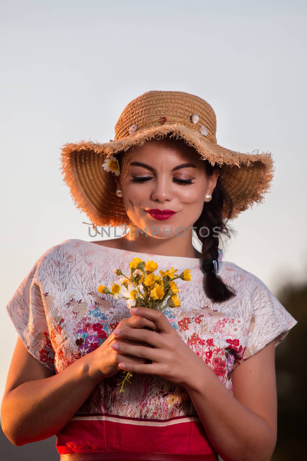 Vintage girl on the countryside with wicker hat with bouquet of flowers.