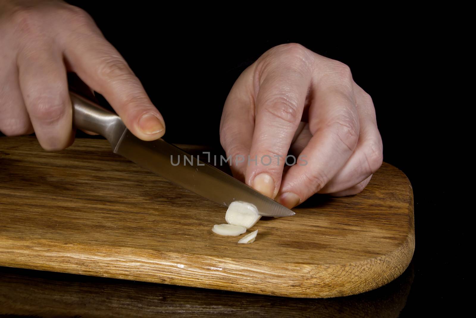 Woman chopping garlic with a knife on a wooden board
