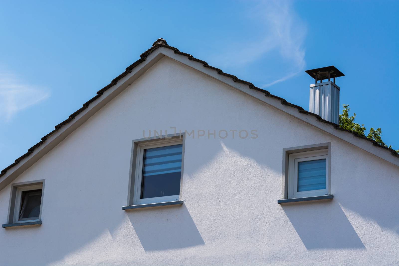 Gable side of a multi-family house of the 60s after modernization, against blue sky.