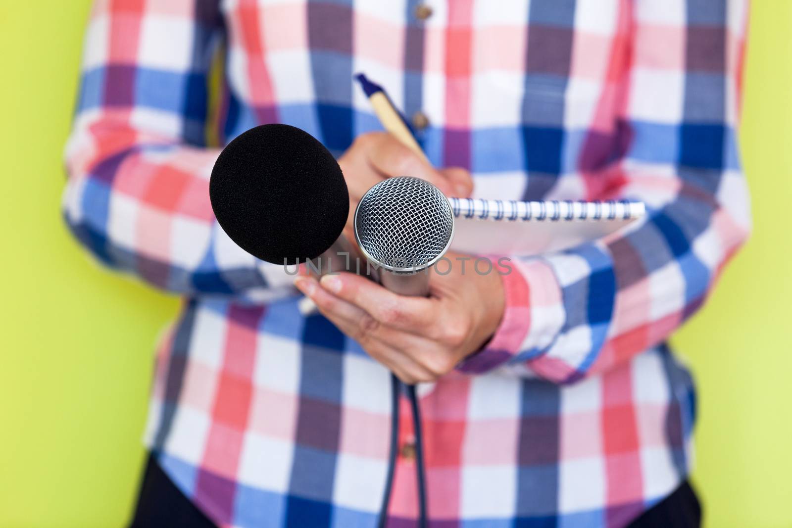 Female reporter at news conference, writing notes, holding microphones