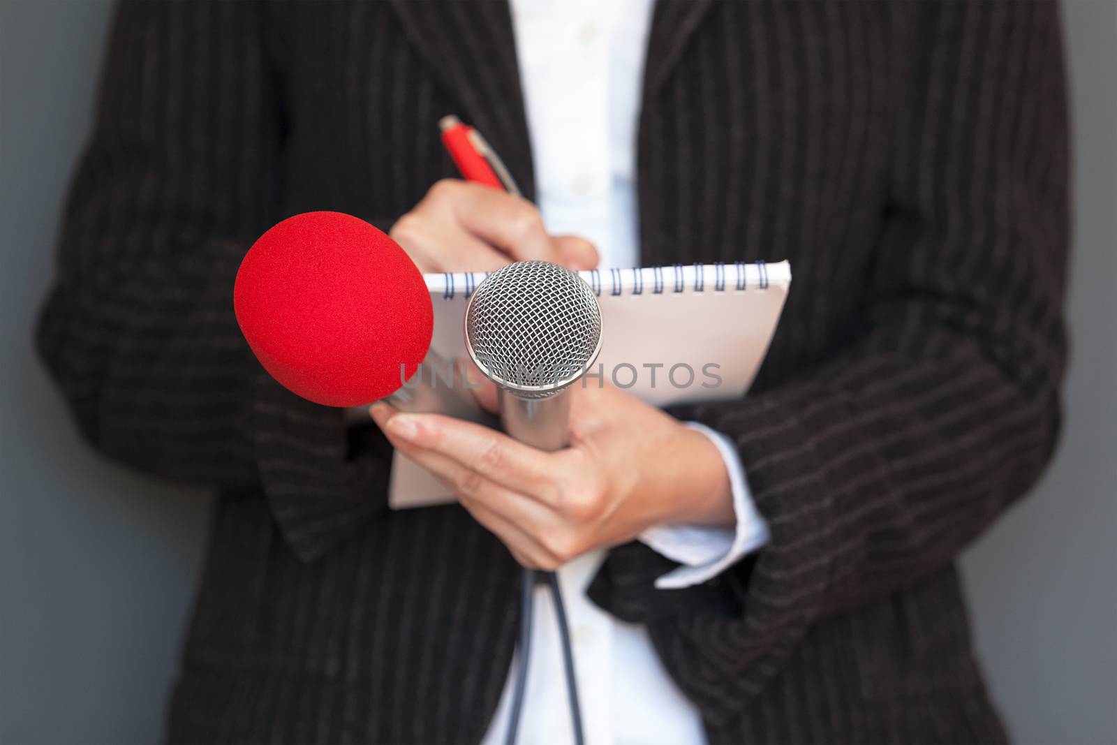 Female reporter at news conference, writing notes, holding microphones