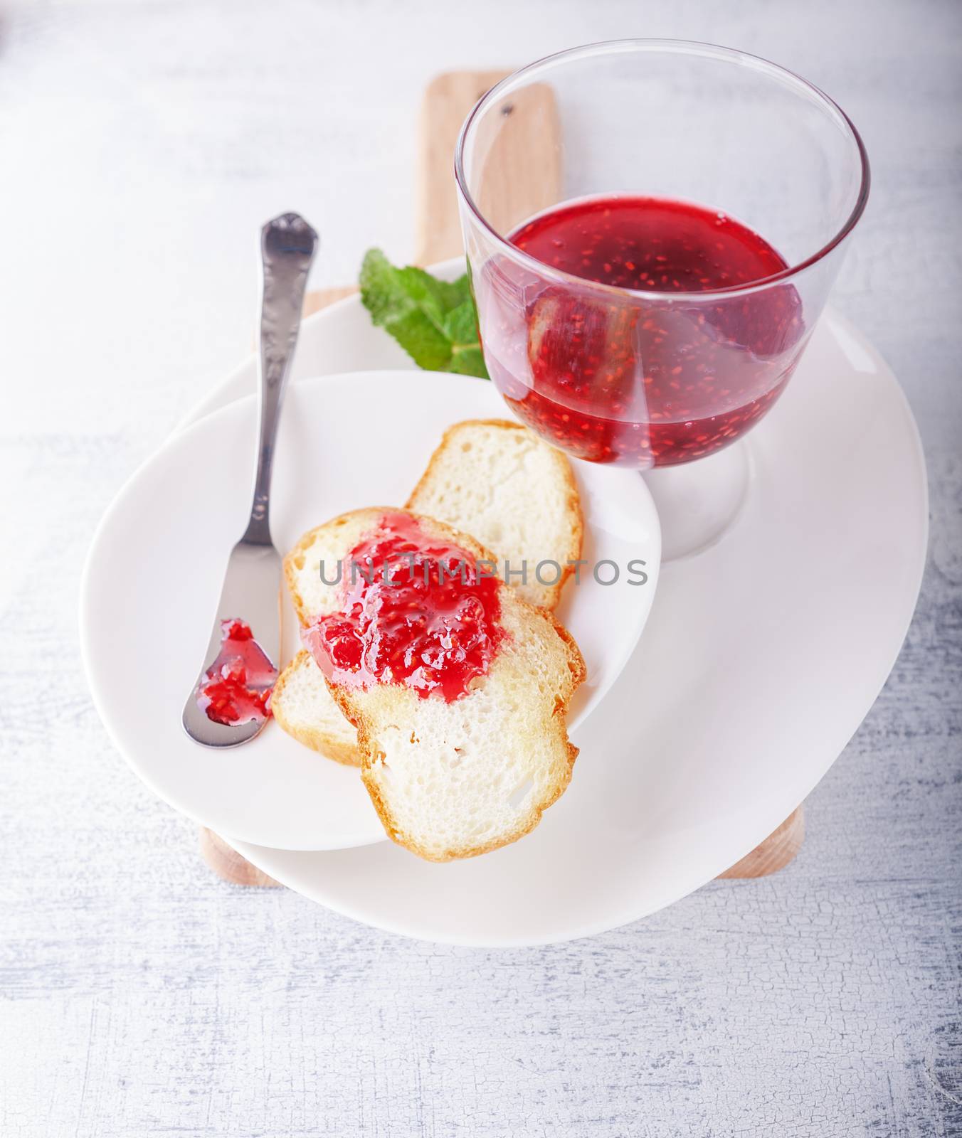 Raspberry jam in bowl with toast on a white surface