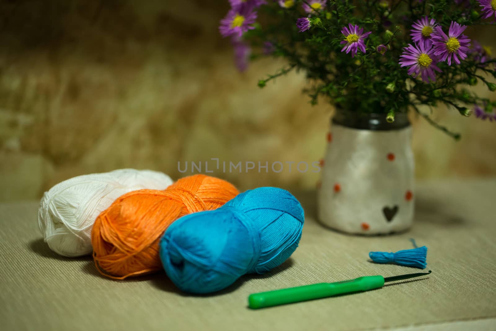 balls of yarn, green crochet hook, and a bouquet of flowers