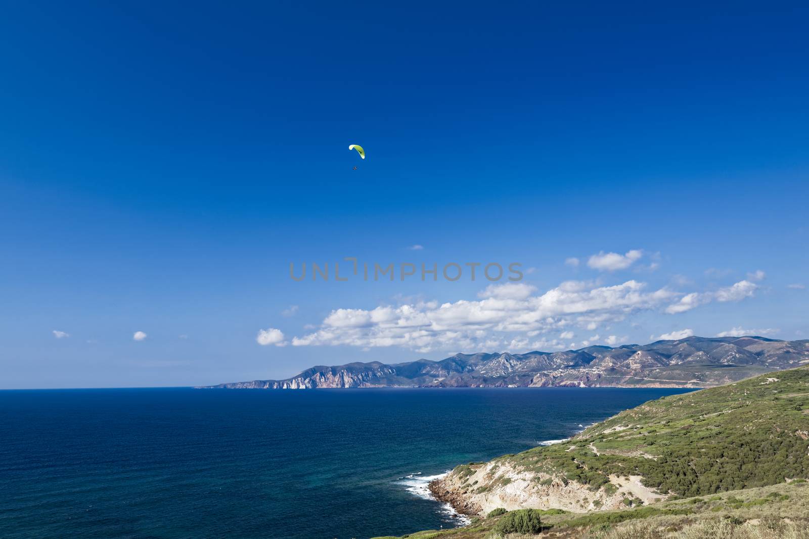 Colorful hang glider in sky over Mediterranean blue sea. Sardinia west coast 