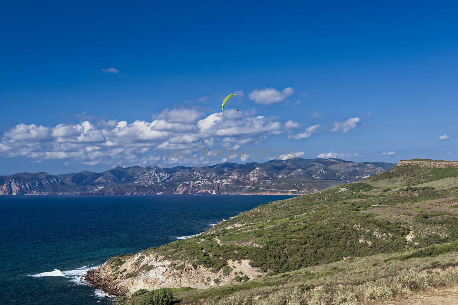 Colorful hang glider in sky over mediterranean blue sea. Sardinia west cost 