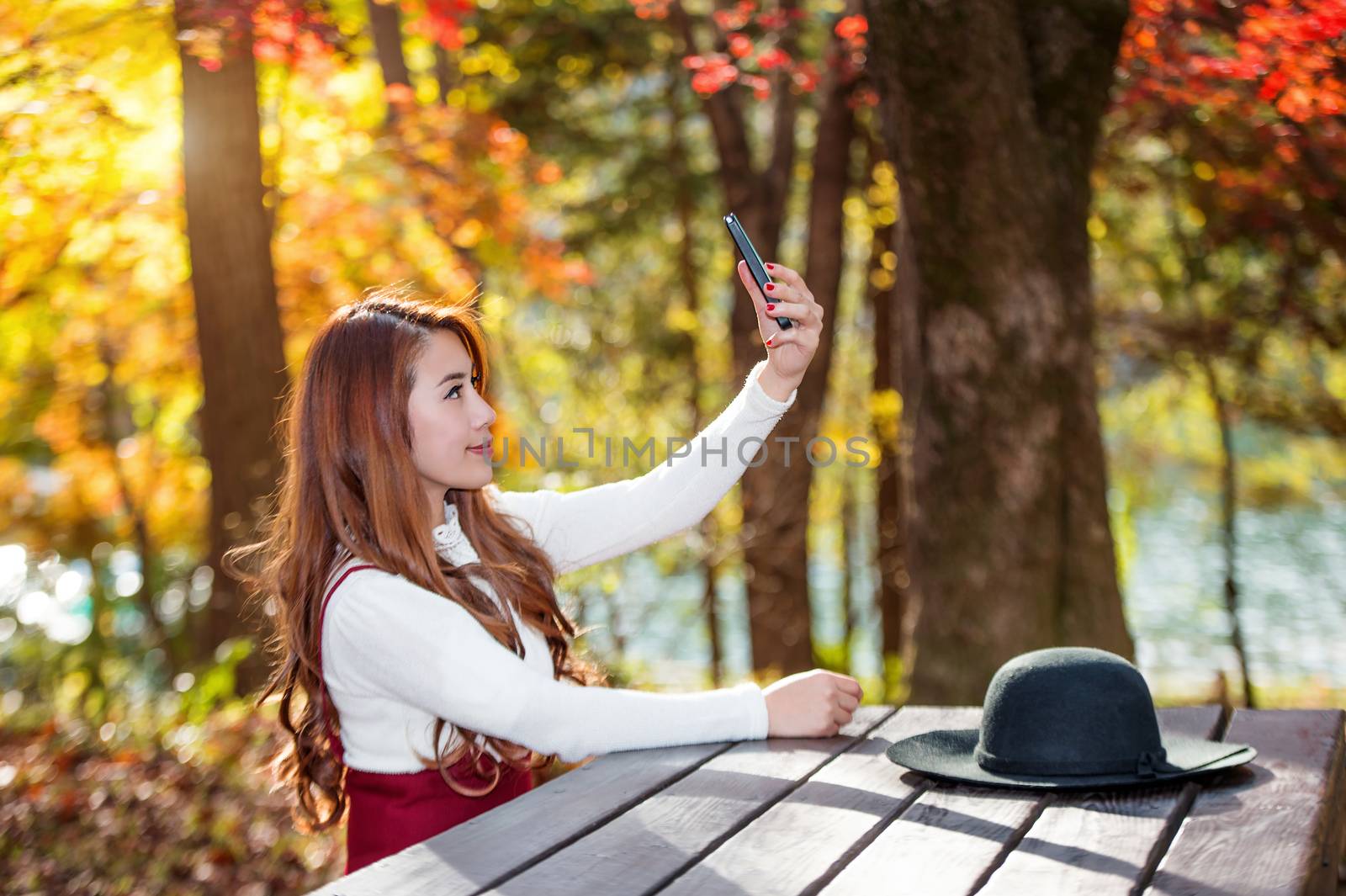 Beautiful woman in fall forest park taking selfie self photo with smartphone.