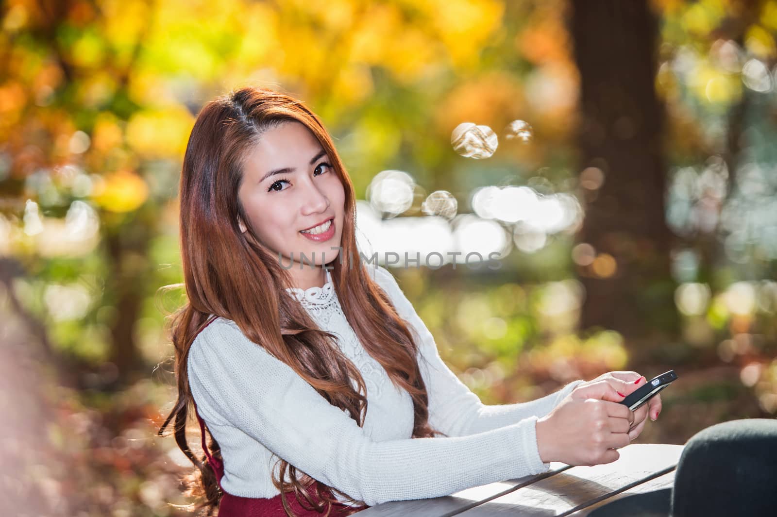 Beautiful woman smiling and hand holding smartphone in fall forest park.
