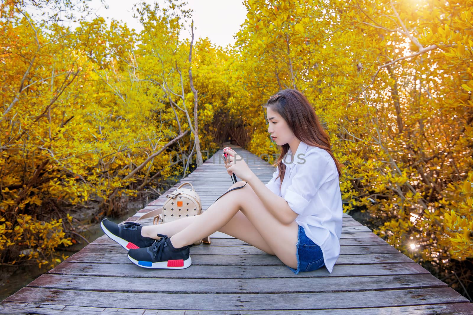 Girl sitting alone and hand holding camera on a the wooden bridge in autumn. by gutarphotoghaphy