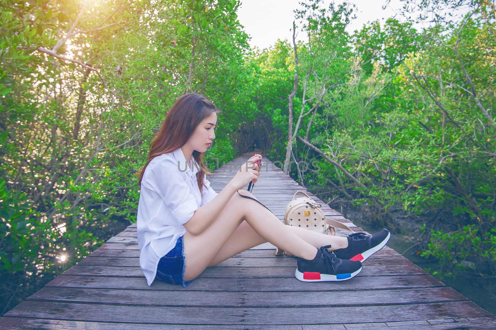 Girl sitting alone and hand holding camera on a the wooden bridge.