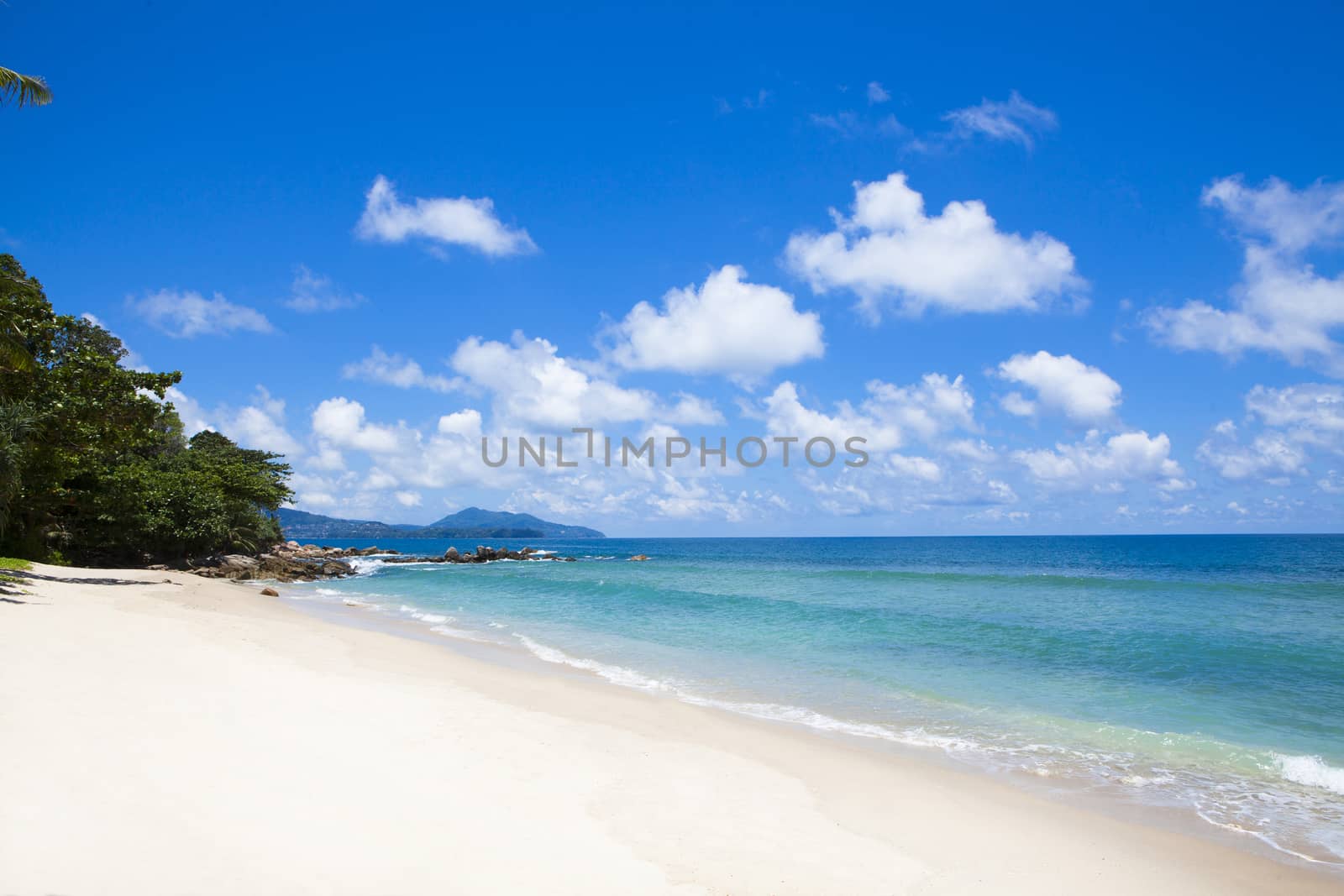 Tropical beach scenery at Andaman sea in Phuket, Thailand. Exotic sea view with people relaxing on vacation at tropical summer paradise beach of Phuket island with sunny sky and clouds on horizon