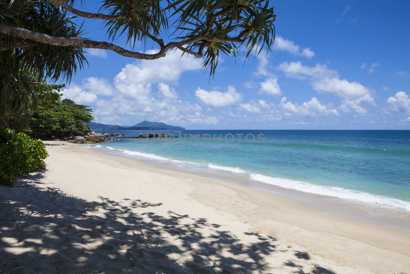 Tropical beach scenery at Andaman sea in Phuket, Thailand. Exotic sea view with people relaxing on vacation at tropical summer paradise beach of Phuket island with sunny sky and clouds on horizon