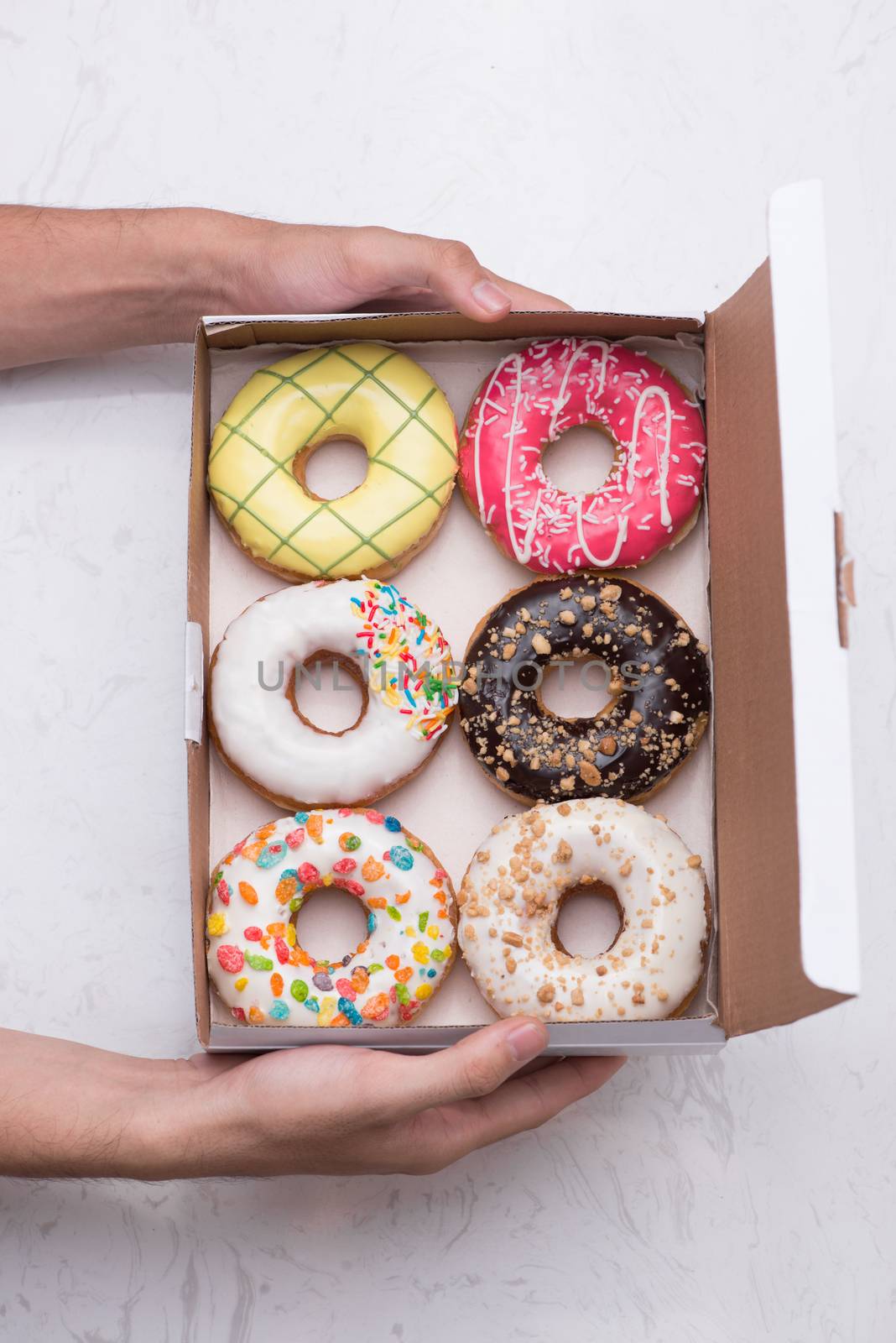 Hand holding colorful round donuts in the box