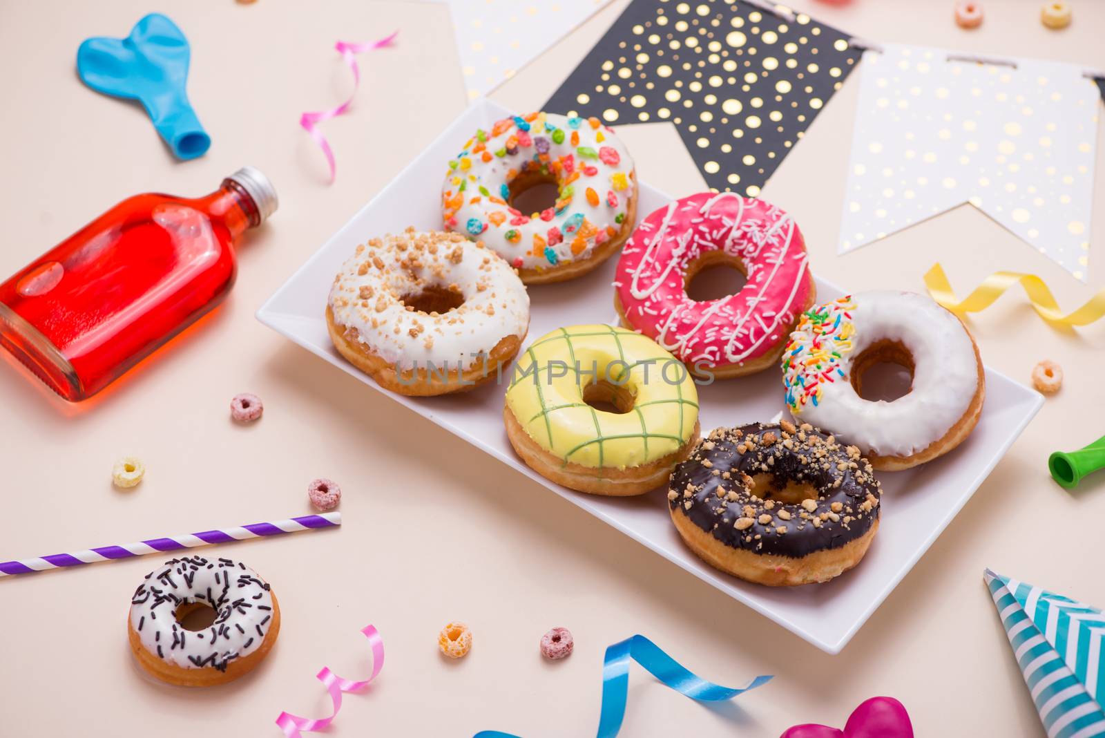 Party. Different colourful sugary round glazed donuts and bottles of drinks on light color background.
